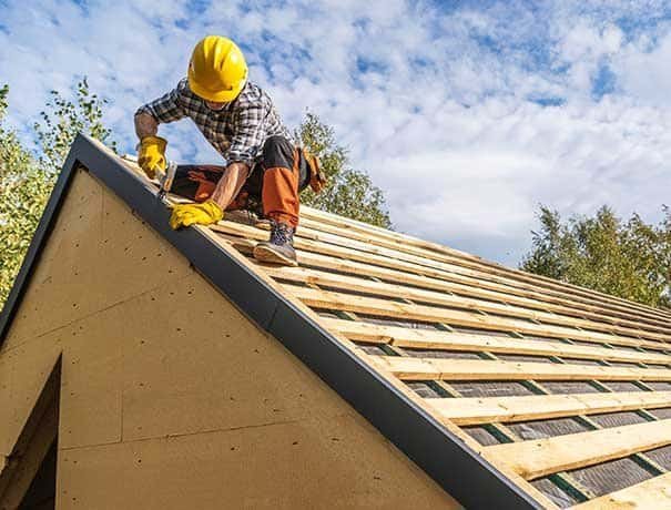 Roofing worker installing shingles on a house roof with safety gear.