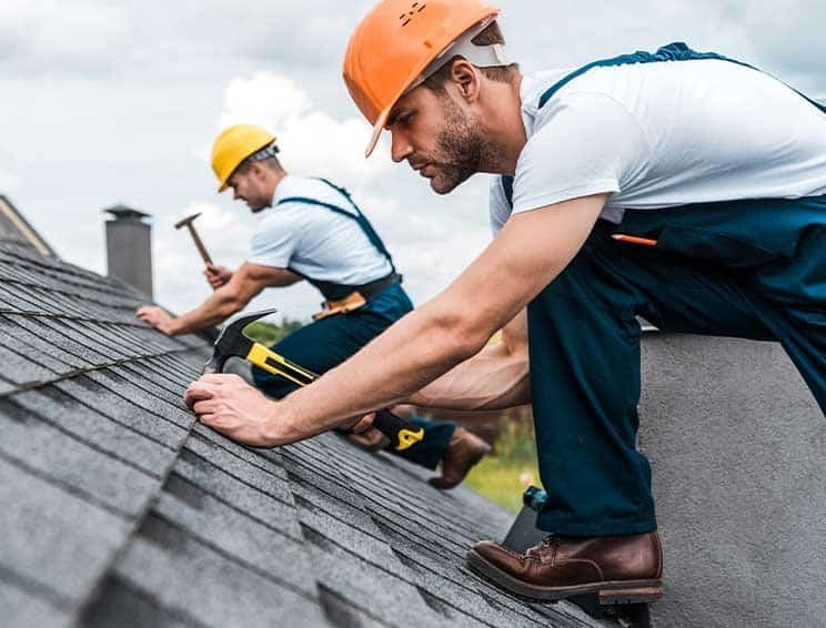 Roofing professionals inspecting and repairing a roof with safety gear.