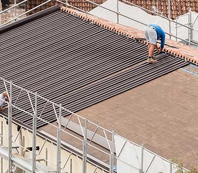Roofing technician installing metal roofing panels on residential home.