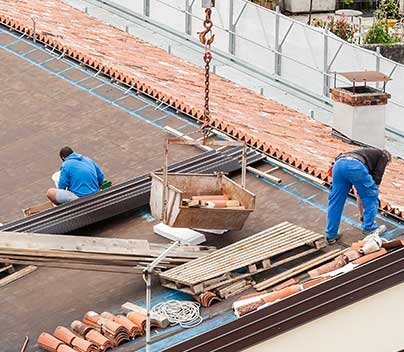 Roofing workers installing tiles on a residential roof with safety railings.