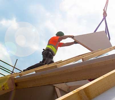 Construction worker installing roofing sheet on wooden roof frame.