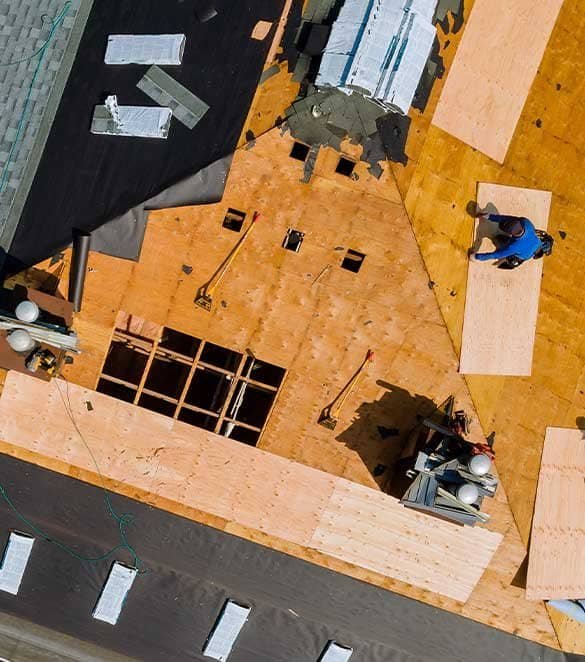 Construction workers building a roof with plywood sheets and tools.